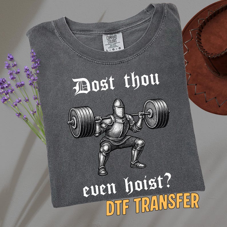 May include: Dark gray t-shirt with a graphic of a knight lifting weights, with the text "Dost thou even hoist?" and "DTF TRANSFER". The shirt has a crew neck and a Comfort Colors tag.