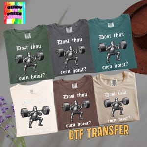 May include: Six different-colored t-shirts are displayed, each featuring a graphic of a knight lifting weights with the text "Dost thou even hoist?". The shirts are in shades of green, gray, brown, and cream, with the words "DTF TRANSFER" at the bottom.