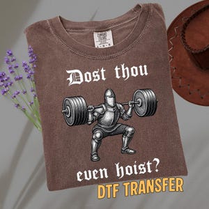 May include: Brown t-shirt with the text "Dost thou even hoist?" and a graphic of a knight lifting weights. The shirt is a Comfort Colors brand and has a vintage look.