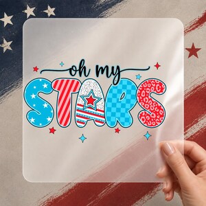 May include: A clear, square sticker featuring the words "oh my STARS" in a vibrant, patriotic design. The word "STARS" is in blue, red, and white with star and pattern details. The background features a flag.