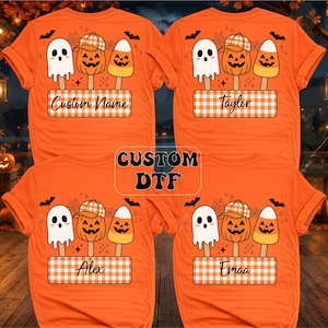May include: Four orange t-shirts featuring a graphic of a ghost, a pumpkin wearing a plaid hat, and a candy corn on sticks. Below the graphic is a rectangular plaid patch with the text Custom Name, Taylor, Alex, or Emaa. A central box reads CUSTOM DTF.