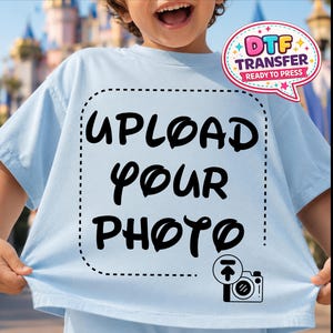 May include: Pale blue t-shirt featuring the words "UPLOAD YOUR PHOTO" in black, within a dotted square. A DTF transfer label is in the upper right. A camera icon is in the lower right corner.