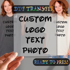 May include: A clear sheet with the text "DTF TRANSFER" in rainbow colors at the top. The text "CUSTOM LOGO TEXT PHOTO" is in black and white with a whimsical font. The sheet is held in front of two t-shirts, one gray and one white, both with the text "CUSTOM LOGO TEXT PHOTO" printed on them.