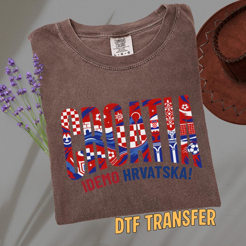 May include: Brown t-shirt with the word "CROATIA" in red, white, and blue, with various Croatian flag-inspired designs. The text "IDEMO HRVATSKA!" is below the word "CROATIA". The words "DTF TRANSFER" are at the bottom.