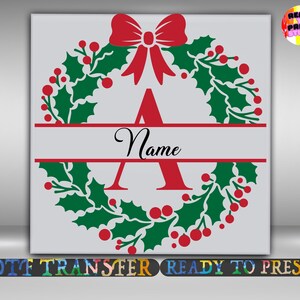 May include: A Christmas-themed design featuring a wreath of green holly leaves and red berries, with a red bow at the top. A red letter "A" and the word "Name" are centered. The design is on a light gray background.