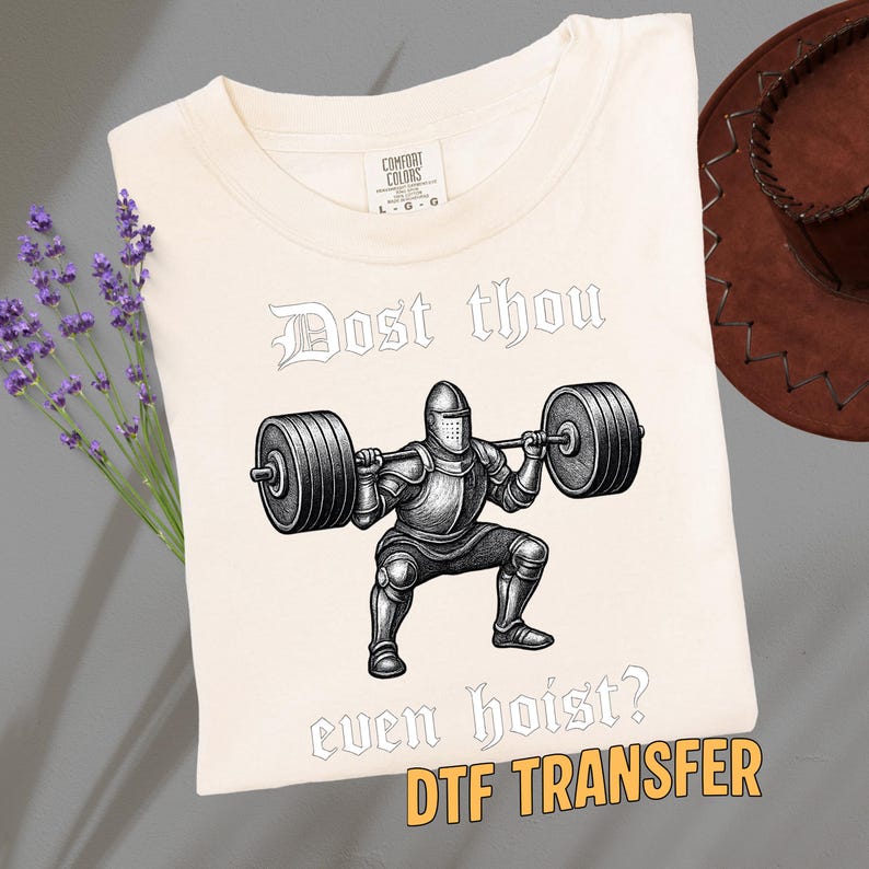 May include: Cream-colored t-shirt featuring a black and white illustration of a knight lifting weights, with the text "Dost thou even hoist?" and "DTF TRANSFER". The shirt has a Comfort Colors tag.