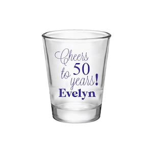 May include: Clear glass shot glass with the text "Cheers to 50 years! Evelyn" printed in purple.