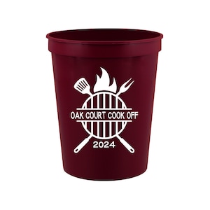 May include: A maroon plastic cup with a white design of a grill, spatula, and fork. The text "OAK COURT COOK OFF 2024" is printed on the cup.