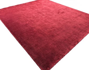Puede incluir: Una alfombra rectangular en un tono rojo carmesí profundo y sólido. La superficie presenta una textura densa de pelo corto con sutiles variaciones en el reflejo de la luz sobre la tela, creando una apariencia suave y uniforme en toda la pieza.