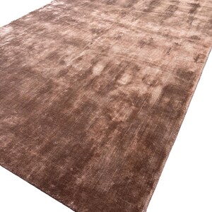 May include: A large, rectangular rug in shades of brown and tan. The rug has a soft, plush texture and a subtle sheen, creating a luxurious appearance. The color variations give the rug a slightly mottled effect.
