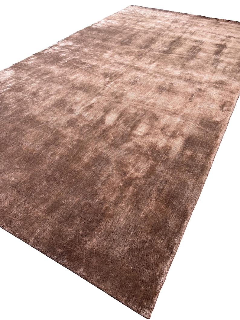May include: A large, rectangular rug in shades of brown and tan. The rug has a soft, plush texture and a subtle sheen, creating a luxurious appearance. The color variations give the rug a slightly mottled effect.