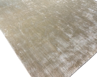 May include: A rectangular area rug featuring a solid, muted gold and beige color palette. The surface displays a distinct, high-low pile texture with a shimmering, distressed finish that creates varied light reflections across the entire fabric.