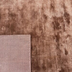 May include: A close-up of a brown rug with a soft, textured surface. The rug has a plush appearance and a contrasting border. The color is a warm, earthy tone, suitable for home decor.