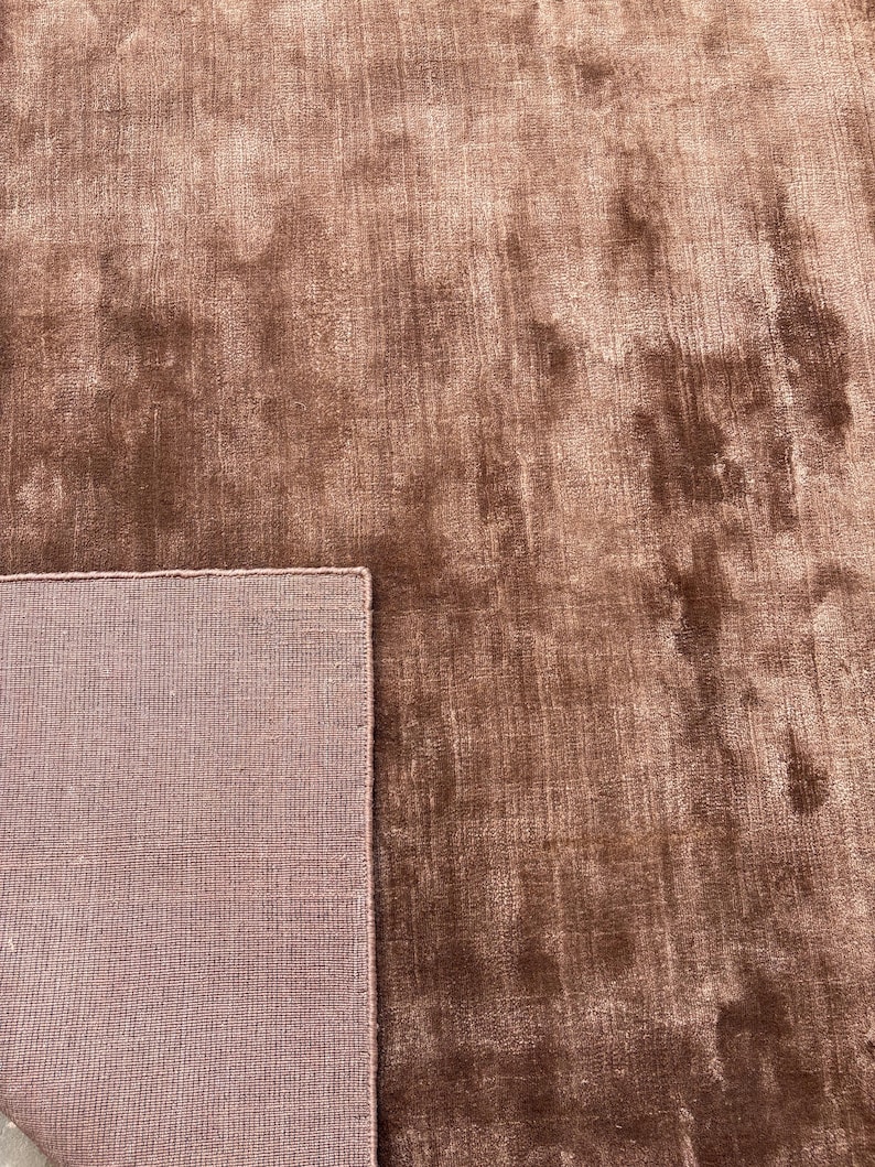 May include: A close-up of a brown rug with a soft, textured surface. The rug has a plush appearance and a contrasting border. The color is a warm, earthy tone, suitable for home decor.