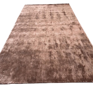 May include: A large, rectangular brown rug with a soft, textured surface. The rug has a subtle sheen and a gradient of light and dark brown tones. The rug is suitable for a living room or bedroom.