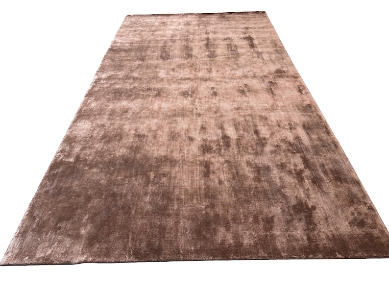 May include: A large, rectangular brown rug with a soft, textured surface. The rug has a subtle sheen and a gradient of light and dark brown tones. The rug is suitable for a living room or bedroom.