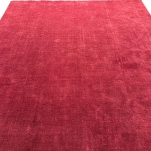 Puede incluir: Una alfombra grande y rectangular en un tono rojo liso. La alfombra tiene un aspecto suave y texturizado, con sutiles variaciones de color y un aspecto ligeramente desgastado. La alfombra es adecuada para una sala de estar o un dormitorio.