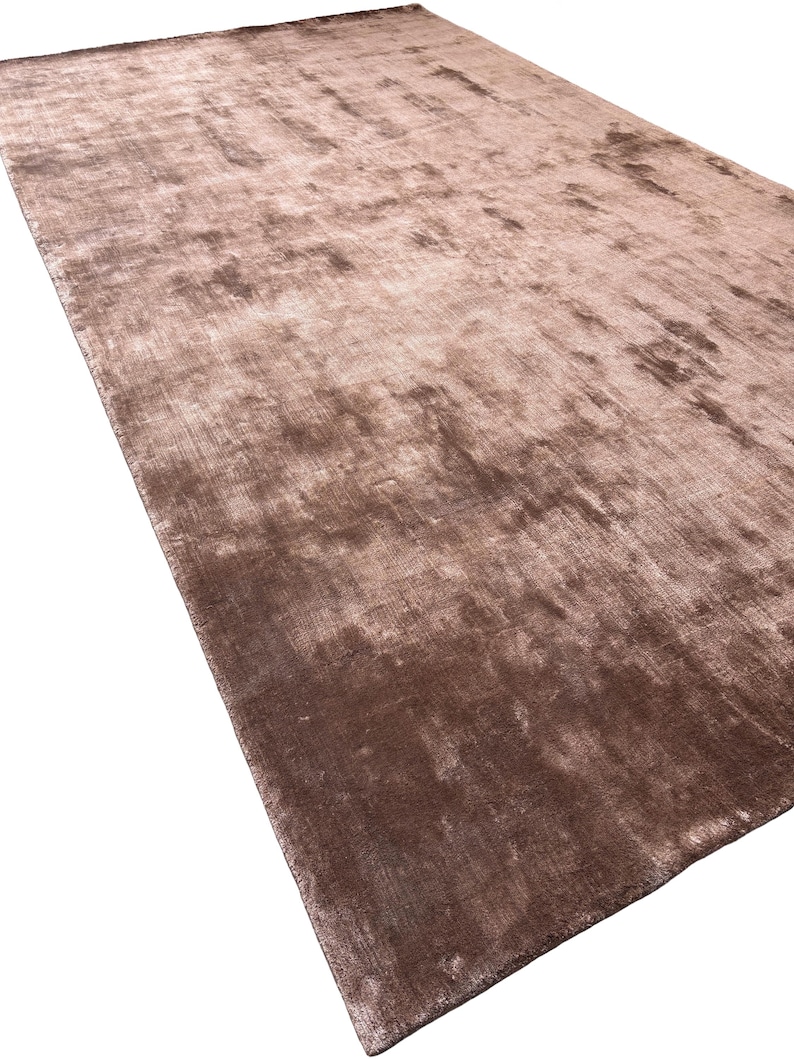 May include: A large, rectangular rug in shades of brown and tan. The rug has a soft, textured appearance with subtle variations in color, creating a plush and inviting look. The rug's design is simple, making it suitable for various interior styles.