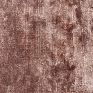 May include: A close-up shot of a dusty rose-colored rug with a textured, distressed appearance. The rug has a soft, velvety feel with variations in color, creating a vintage aesthetic. The rug's surface shows subtle patterns and a worn look.