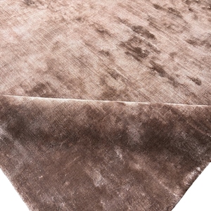 May include: A close-up of a section of a brown velvet fabric. The fabric has a soft, textured appearance with subtle variations in color, creating a luxurious look. The fabric is folded over, revealing the underside.