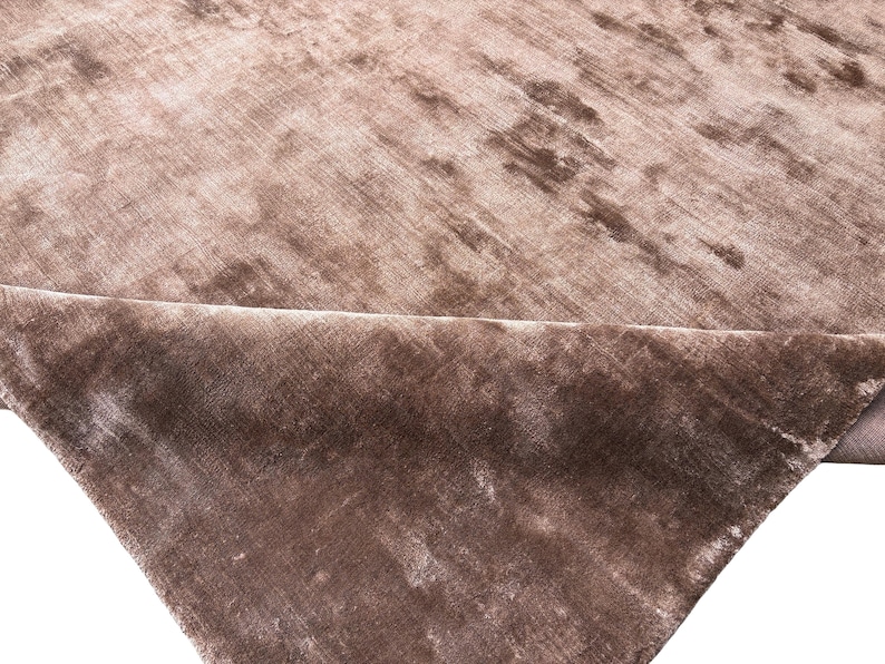 May include: A close-up of a section of a brown velvet fabric. The fabric has a soft, textured appearance with subtle variations in color, creating a luxurious look. The fabric is folded over, revealing the underside.