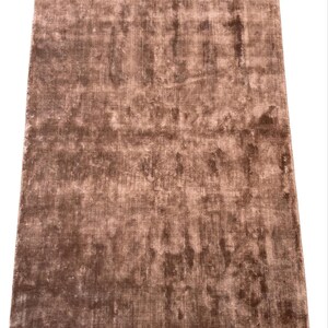 May include: A rectangular, brown rug with a textured surface. The rug has a soft, plush appearance and a subtle sheen. The color is a warm, earthy tone, suitable for home decor.