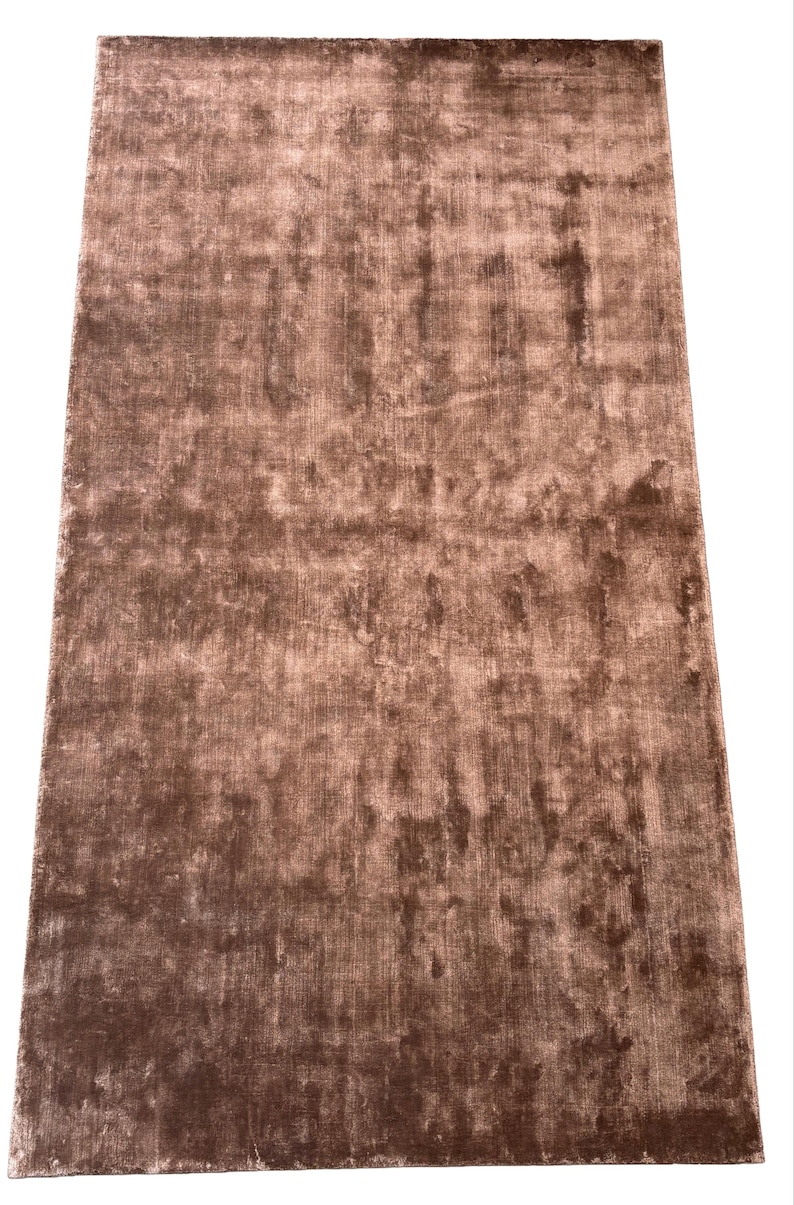 May include: A rectangular, brown rug with a textured surface. The rug has a soft, plush appearance and a subtle sheen. The color is a warm, earthy tone, suitable for home decor.