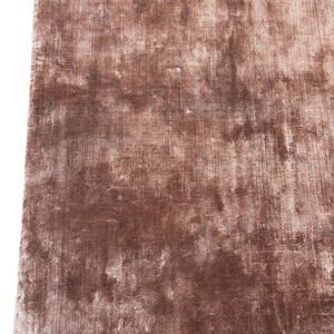 May include: A close-up shot of a rectangular, plush rug in a muted, dusty rose color. The rug has a soft, textured appearance with subtle variations in tone, creating a luxurious feel. The fibers appear dense and slightly reflective, suggesting a high-quality material.