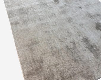 Puede incluir: Una alfombra rectangular grande en una paleta de colores neutros. La alfombra tiene un aspecto suave y texturizado con sutiles variaciones de tono, creando una sensación de profundidad. El color es una mezcla de tonos gris-marrón claros y medios.
