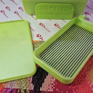 May include: A lime green diamond painting docking station set. The set includes a tray with black lines, a lid, and a container with the text "CHAMELEON DOCKING STATION". The items are on a patterned surface.