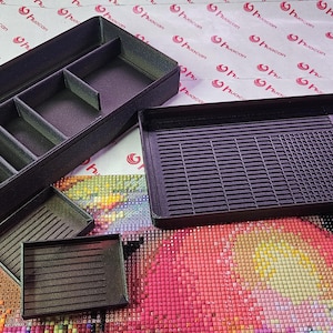 May include: A set of black plastic craft organizers, including a divided tray, a rectangular tray with a ridged surface, and two smaller trays. The organizers are designed for storing and organizing craft supplies.