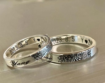 Op de afbeelding: Twee zilveren ringen met gegraveerde vingerafdrukken en de datum "2023.8.5 Y♥Z" op de ene ring en het woord "Yang" op de andere.