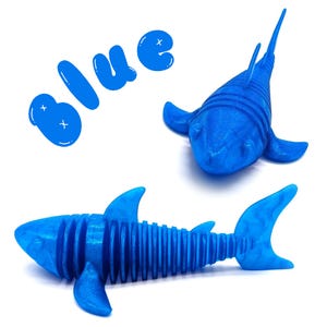 May include: Two blue shark toys and the word "blue" in a playful font. One shark is a detailed model with fins and a tail. The other shark has a streamlined design. The toys are on a white background.