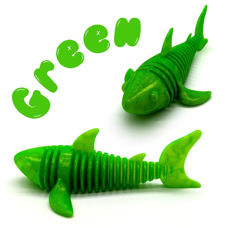 May include: Two articulated green shark toys on a white background. The word "GREEN" is written in green bubble letters above the sharks. The sharks have fins, tails, and segmented bodies.