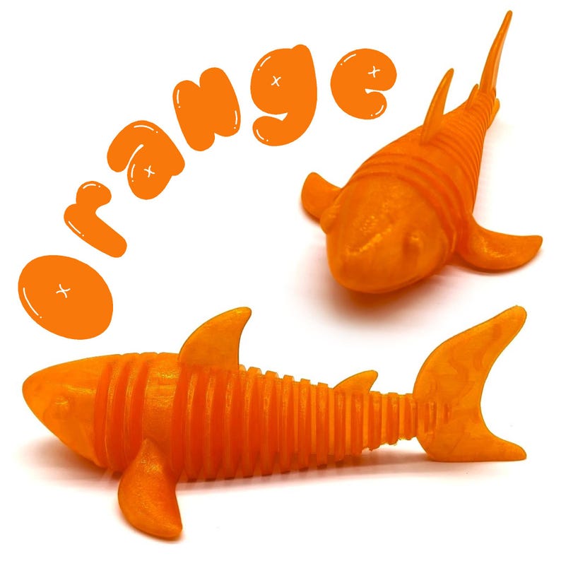 May include: Two orange shark-shaped toys with fins and segmented bodies are displayed on a white background. The word "ORANGE" is written above the sharks in orange bubble letters. One shark is positioned horizontally, and the other is vertical.