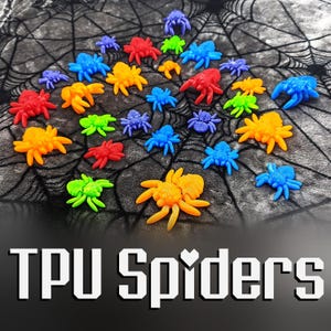 Puede incluir: Una colección de arañas impresas en 3D de colores, hechas de plástico TPU. Las arañas están dispuestas en círculo sobre una superficie texturizada negra y gris. Las arañas son de varios colores, incluyendo rojo, naranja, amarillo, verde, azul y morado.