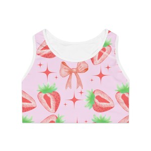 May include: A pink tank top with a white trim and a pattern of strawberries, bows, and stars.