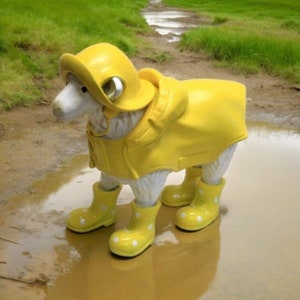 Könnte beinhalten: Eine gelbe Keramikskulptur eines Hundes, der einen gelben Regenmantel und gelbe Gummistiefel mit weißen Punkten trägt. Der Hund steht in einer Pfütze.