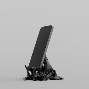 May include: A black smartphone rests on a black, organically shaped phone stand. The stand has a textured, abstract design, and the phone is angled slightly. The background is a solid, neutral gray.