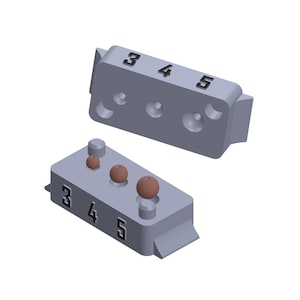 May include: A gray plastic mold with three round depressions, labeled 3, 4, and 5. The mold is open, revealing three brown beads inside.