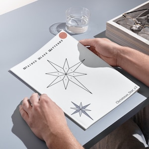May include: A white sheet of paper with the title "Stained Glass Patterns" and a black and white illustration of a Christmas star with numbered sections. The text "Christmas_Star_v2" is at the bottom of the page.