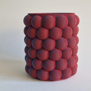 May include: A red and purple cylindrical planter with a textured surface made of small, rounded bumps.
