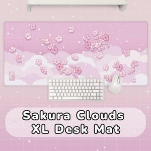 May include: Pink XL desk mat with a Sakura Clouds design. The mat features a light pink background with white clouds and pink cherry blossom flowers. A white keyboard and mouse are on the mat.