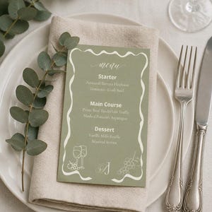 Puede incluir: Una tarjeta de menú rectangular de color verde salvia con un borde ondulado blanco, que presenta el texto menu, Starter, Main Course y Dessert, junto con ilustraciones de líneas de copas de vino y uvas, sobre una servilleta de lino beige.
