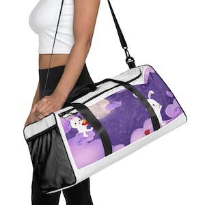 Könnte beinhalten: Eine weiße Sporttasche mit einem violetten Nachthimmel-Motiv, das einen Vollmond, Sterne und zwei weiße Cartoon-Hasen auf violetten Wolken zeigt. Die Tasche verfügt über schwarze Trageriemen, eine schwarze Netzseitentasche und einen schwarzen Reißverschluss.