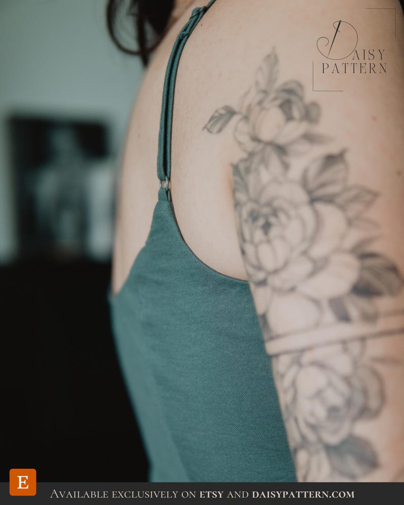May include: A dark teal tank top featuring thin adjustable shoulder straps with metal sliders. The garment has a simple neckline and is shown from a side angle, revealing the fabric texture and the solid, deep green color of the material.