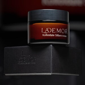 Könnte beinhalten: Ein braunes Glas mit schwarzem Deckel, beschriftet mit "LADEMOR Kolloidale Silbercreme", steht auf einer schwarzen Schachtel. Das Etikett des Glases ist in weißer Schrift. Auf der Schachtel stehen auch der Marken- und Produktname.