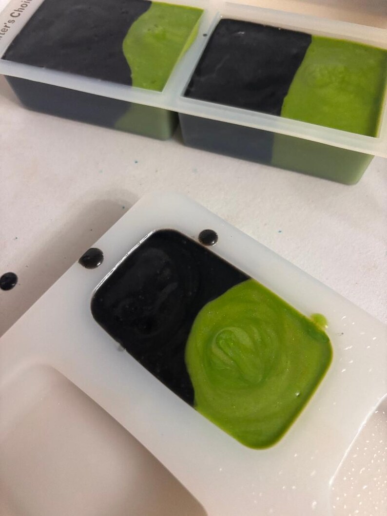 Peut inclure: Gros plan sur la fabrication de savon. Moules &agrave; savon rectangulaires avec du savon noir et vert. Le savon est en cours de versement dans les moules. Le savon est un m&eacute;lange de couleurs noir et vert.