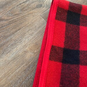 Może przedstawiać: Złożony czerwono-czarny koc w kratę. Koc ma klasyczny wz&oacute;r w kratę w odważnych czerwonych i czarnych kwadratach. Krawędź koca jest obszyta jednolitym czerwonym obramowaniem.