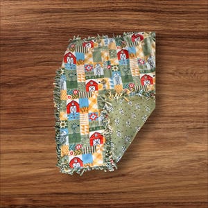 Op de afbeelding: Een groene en rode patchwork babydeken met een boerderijthema. De deken heeft een rafelige rand en is gemaakt van zacht, knuffelig materiaal.